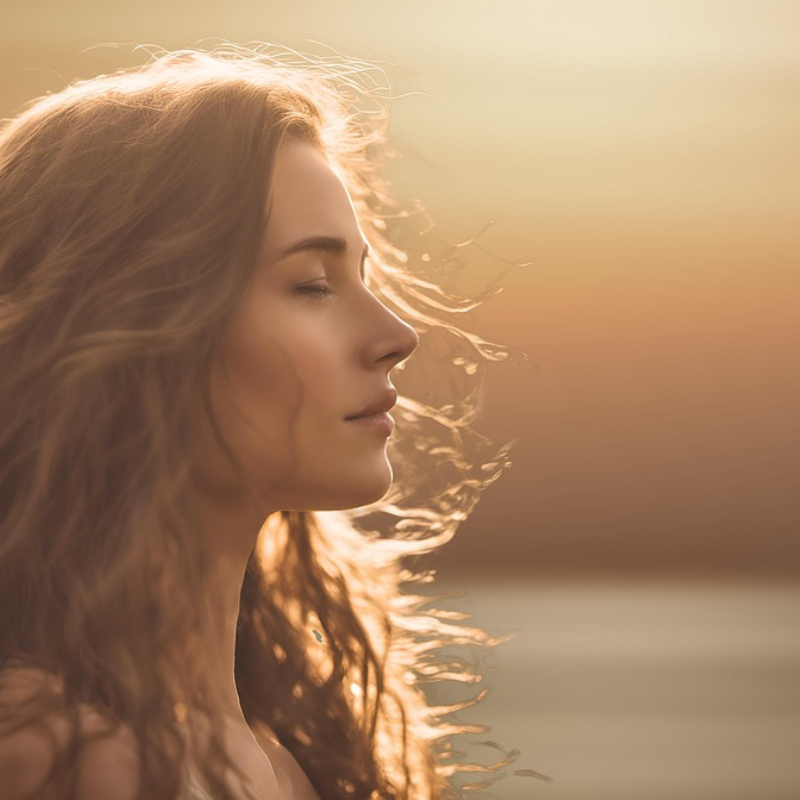 Fiatal nő oldalnézetből, csukott szemmel, naplementében.